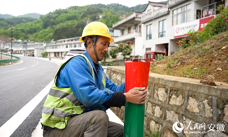 大湾村村民陶元佳正在路边为护栏张贴反光贴。人民网记者 王锐摄